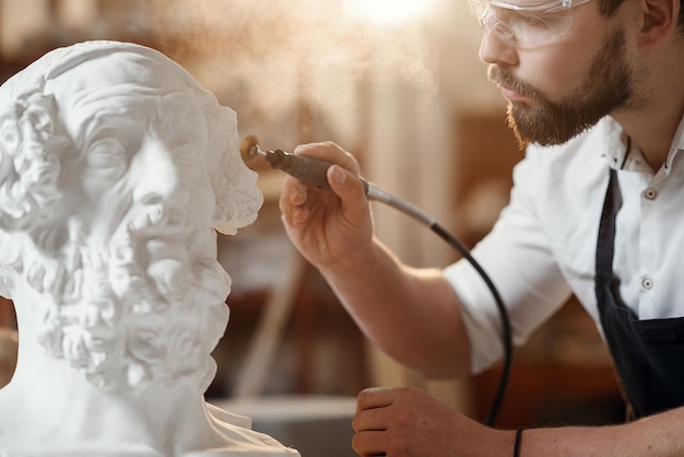 Escultor reparando una escultura de yeso de la cabeza de una mujer en el lugar de trabajo en el área creativa