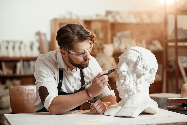 Escultor reparando una escultura de yeso de la cabeza de una mujer en el lugar de trabajo en el área creativa