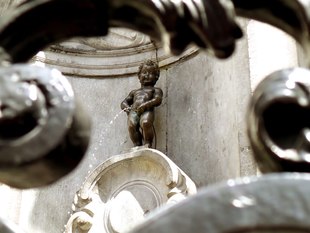 Escultura de bronce de Manneken Pis como vista a través de la valla de hierro