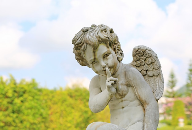 Escultura de cupido en jardín de verano al aire libre.