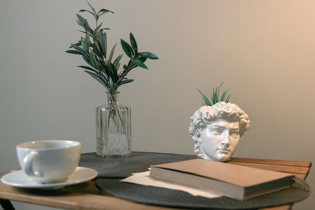 Escultura da cabeça de David na mesa com uma xícara de café e um livro. Interior moderno clássico