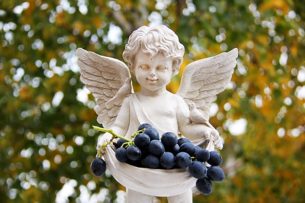 Escultura de menino com asas de anjo segurando suculentas uvas maduras