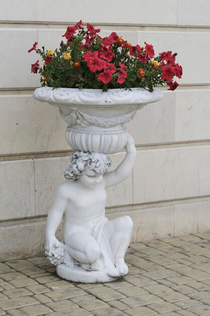 Escultura de um menino com um vaso na cabeça com flores