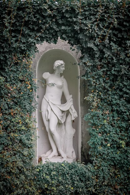 Escultura de jardín Un hermoso pedestal de una mujer en el fondo de una pared verde en el parque Fondo para eventos al aire libre