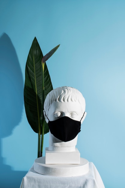 Foto escultura de mármol de figura histórica con máscara médica y hoja.
