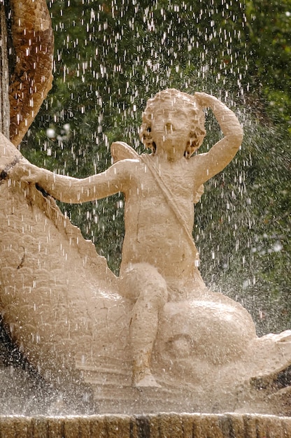 escultura de piedra de un niño apoyado en un pez en una fuente del parque mientras llueve