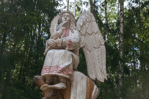 Foto esculturas de madera nacionales bielorrusas en el bosque. ángel de madera en ropa tradicional bielorrusa con un pájaro en sus manos.