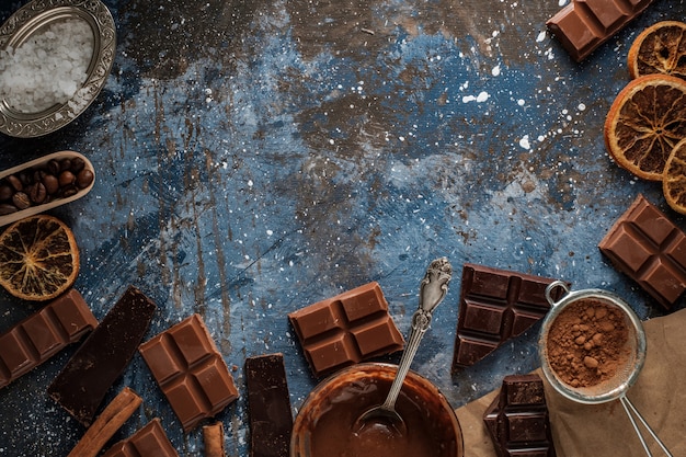 Escuro e barras de chocolate ao leite com fatias de laranja secas, paus de canela e grãos de café na superfície azul,