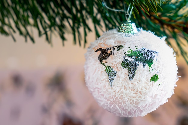 Esfera de vidro de Natal com uma figura na forma de um mapa do mundo pendurado em um ramo de pinheiro