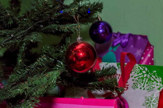 Esfera roja colgando del árbol de Navidad con regalos en el fondo