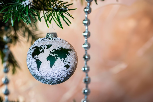 Esfera de vidrio de Navidad con una figura en forma de un mapa del mundo colgando de una rama de pino