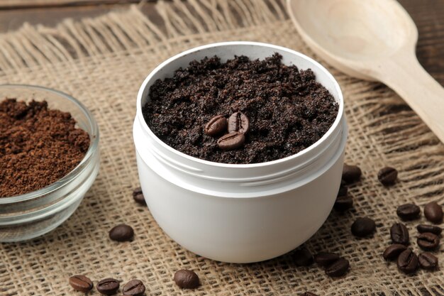 Esfoliante de café caseiro em pote branco para o rosto e corpo e vários ingredientes para fazer esfoliante.