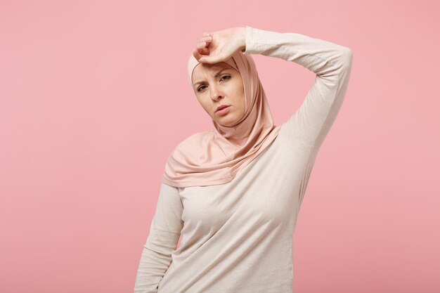 Esgotada jovem muçulmana árabe em roupas leves hijab posando isolado no retrato de estúdio de fundo de parede rosa. Conceito de estilo de vida do Islã religioso de pessoas. Mock up espaço de cópia. Colocando a mão na cabeça.