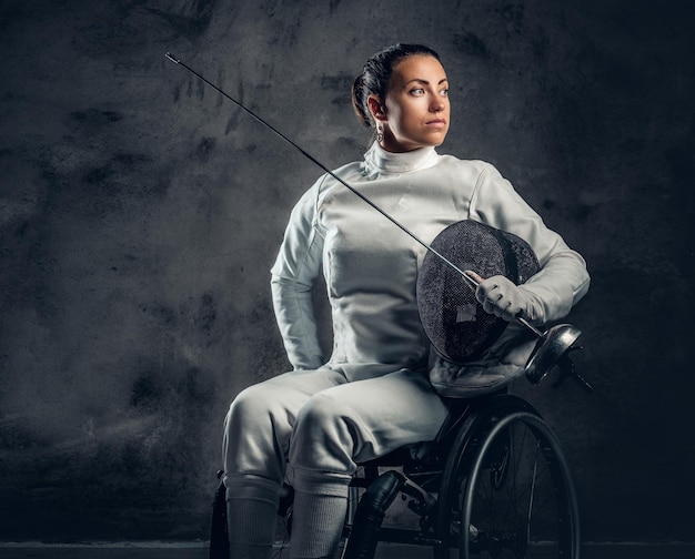 Esgrimista feminina em cadeira de rodas com máscara de segurança de um rosto segurando florete, efeito de poeira na imagem.