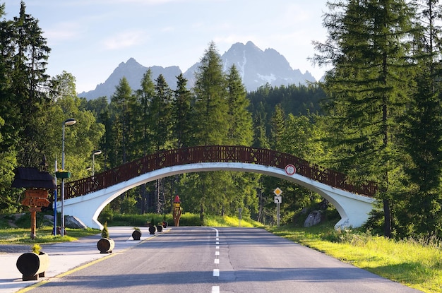 ESLOVÁQUIA, SHTRBSVE PLESO - 29 DE JUNHO: paisagem do verão com a estrada em um resort de montanha e uma ponte pedonal. Tatras, Eslováquia