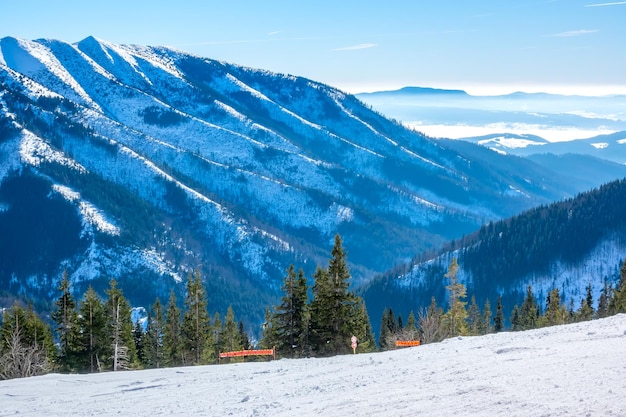 Eslováquia. estância de esqui de inverno jasna. tempo ensolarado e céu azul ao longo de uma pista de esqui vazia. picos de montanhas e neblina no horizonte