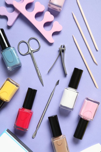 Esmalte de unhas e conjunto de ferramentas de pedicura em fundo lila.
