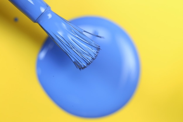 Esmalte de uñas azul gotas azules de esmalte de uñas y pincel sobre fondo amarillo brillante