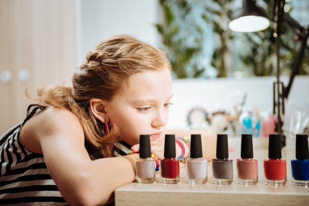 Esmalte de uñas. Elegante atractivo adolescente sentado y mirando colores de esmalte de uñas en el salón de belleza