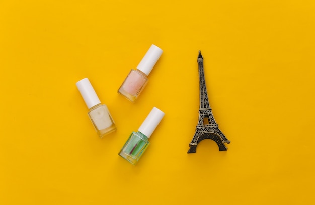 Esmalte de uñas y estatuilla de la torre Eiffel en amarillo. Concepto de belleza