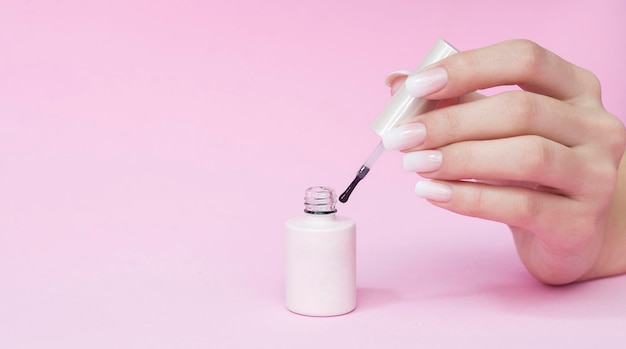 Esmalte de uñas rosa pálido en la mano, primer plano. Fondo rosa. Tonos de cama