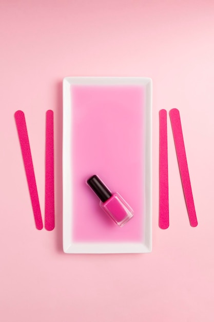 Esmalte de uñas rosa plano sumergido en líquido rosa con limas de uñas rosas y fondo rosa Productos de manicura y pedicura Concepto estético