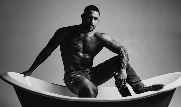 Eso significa que es hora del baño Hombre latino fuerte con tatuaje en el torso musculoso sentado en el baño Hombre hispano atlético bebiendo vino en el baño El vino y el baño son la clave para la relajación para él