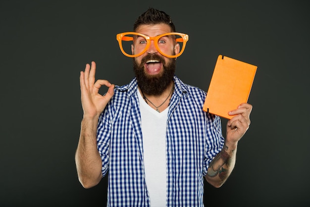 Espacio de copia de portada de libro. El hombre barbudo hipster usa anteojos divertidos y sujeta el bloc de notas o libro. Ilumina tu día. Lee este libro. Sentido cómico y humorístico. Esta historia acaba de alegrarme el día. Libro divertido para relajarse.