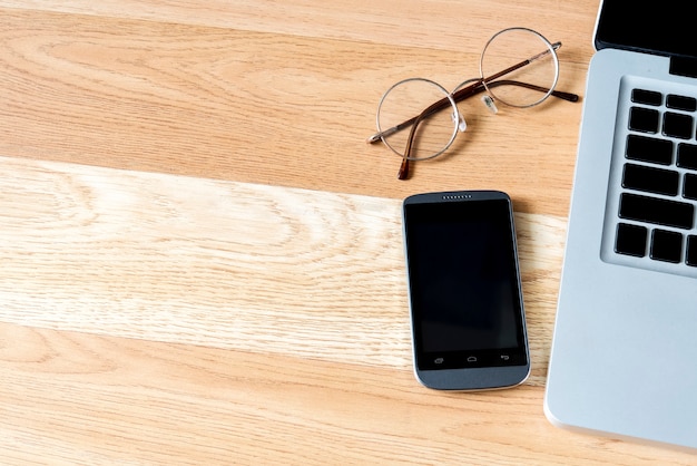 Espacio libre con computadora portátil, vidrio y teléfono inteligente en la mesa de madera