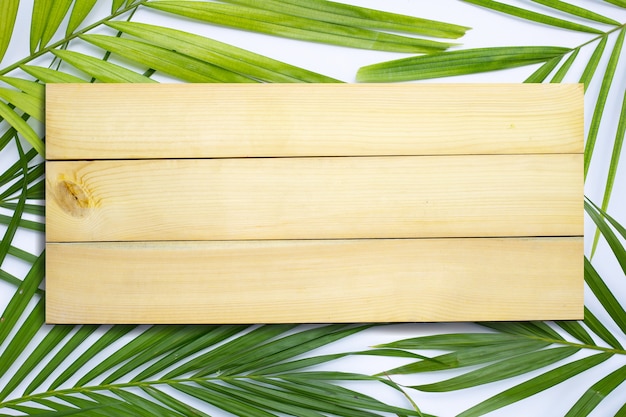 Espacio de madera en hojas de palmeras tropicales sobre superficie blanca