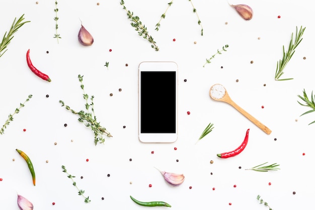 Espacio de texto en blanco de maqueta de smartphone de vista aérea plana endecha sobre fondo blanco con hierbas verdes y especias. Diseño de menú, blog de alimentos, receta, libro de cocina o aplicación de entrega con ingredientes para cocinar