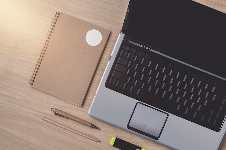 Foto espacio de trabajo con agenda o cuaderno y computadora portátil, bolígrafo, lápiz, pluma de luz alta, clip de metal sobre madera