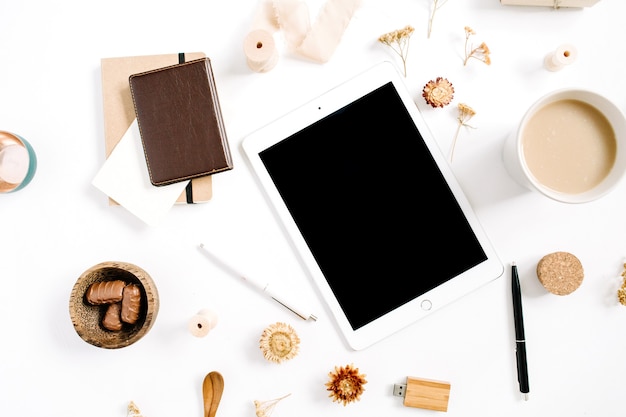 Espacio de trabajo de blogger o autónomo con tableta, taza de café, cuaderno, dulces y accesorios sobre fondo blanco. Escritorio de oficina en casa de estilo marrón minimalista plano, vista superior. Concepto de blog de belleza.