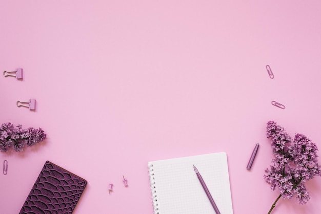 El espacio de trabajo de un bloguero o freelance Lay Flat con un bolígrafo de cuaderno y papelería de ramas lila sobre un fondo lila con un espacio de copia