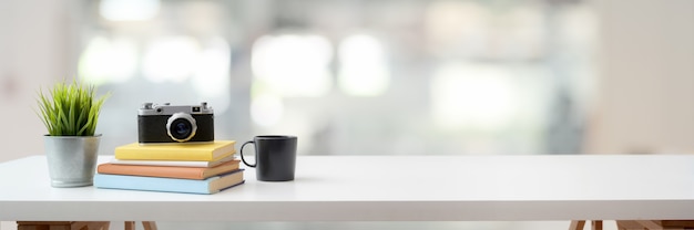 espacio de trabajo con cámara, libros, taza de café y espacio de copia en mesa blanca