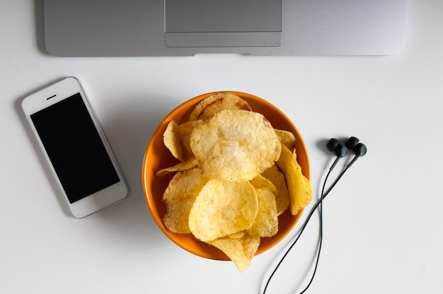 Espacio de trabajo con computadora portátil, papel arrugado y tazón de papas fritas en la mesa de madera. concepto de malos hábitos