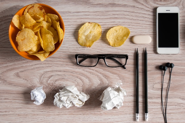 Espacio de trabajo con computadora portátil, papel arrugado y tazón de papas fritas en la mesa de madera. Concepto de malos hábitos