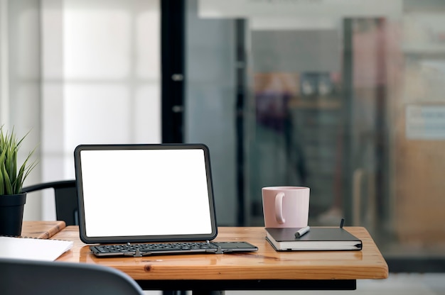 Espacio de trabajo creativo con tableta de pantalla en blanco y teclado en la mesa de madera en la sala de la oficina.