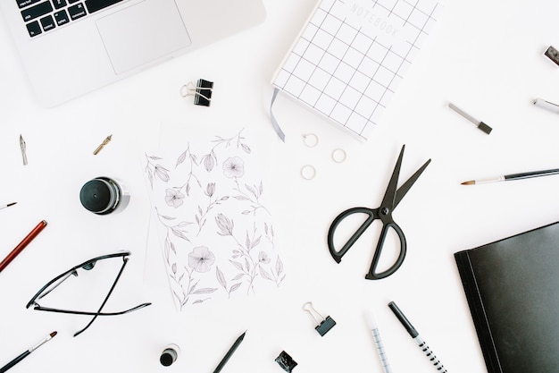 Espacio de trabajo con cuaderno, portátil, tijeras, gafas, bolígrafo en blanco.