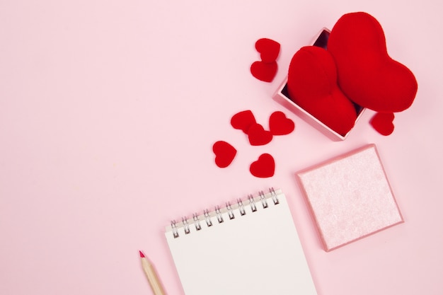 Espacio de trabajo de escritorio femenino con mock up cuaderno en blanco, caja de regalo y corazón rojo en backgr rosa