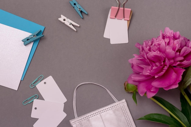 Espacio de trabajo de escritorio femenino de oficina con espacios en blanco de máscara facial de peonía y clips de papel fondo gris