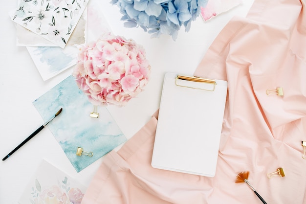Espacio de trabajo de escritorio de oficina en casa de artista de acuarela con portapapeles de espacio de copia, ramo de flores de hortensia pastel, pintura de acuarela, manta peachy