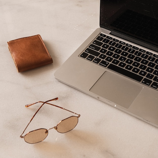 Espacio de trabajo de escritorio de oficina en casa con computadora portátil, gafas de sol, billetera en la mesa de mármol