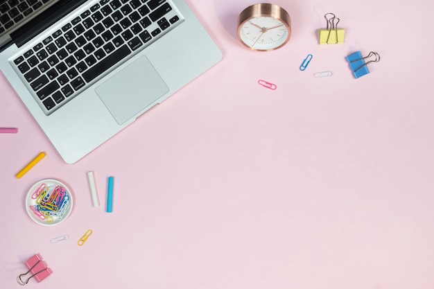 Espacio de trabajo de escritorio de oficina con ordenador portátil y accesorios sobre fondo rosa.