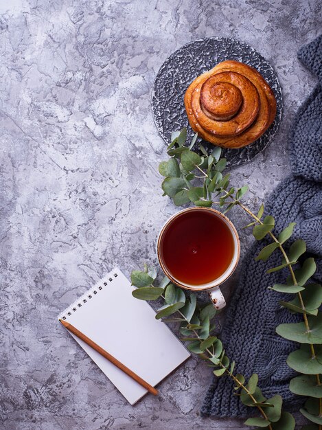 Espacio de trabajo femenino con bollo, taza de té y cuaderno.