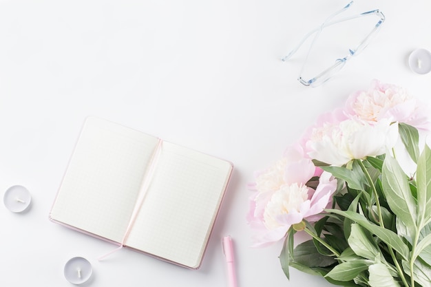 espacio de trabajo femenino con cuaderno abierto en blanco, flores de peonía, anteojos