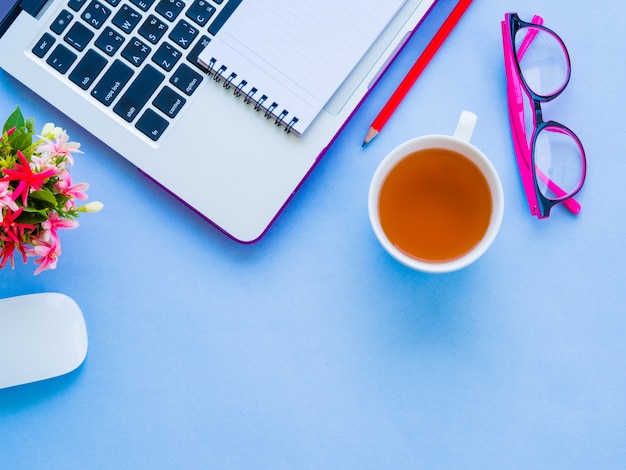 Espacio de trabajo femenino del escritorio con los accesorios de la oficina en fondo azul.