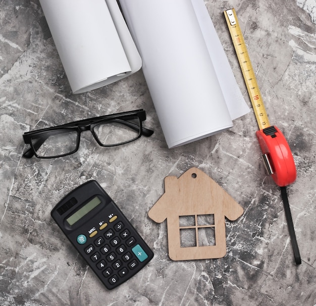 Espacio de trabajo del ingeniero. Casco de construcción, rollos de dibujos, calculadora y gafas, regla sobre fondo de hormigón gris. La construcción de viviendas. Vista superior.