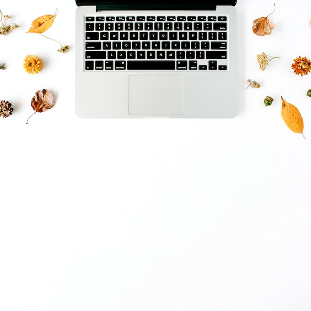 Espacio de trabajo con laptop, bellota, hojas amarillas sobre blanco