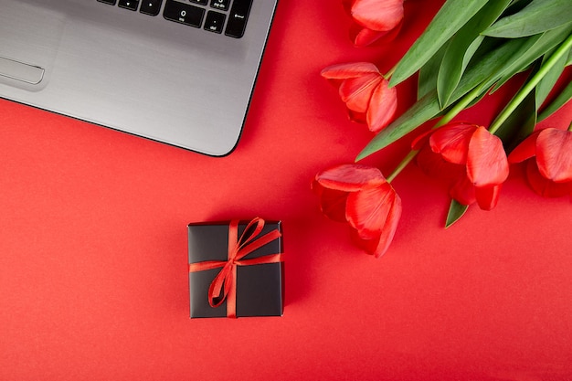 Espacio de trabajo con laptop, tulipanes rojos y caja de regalo.